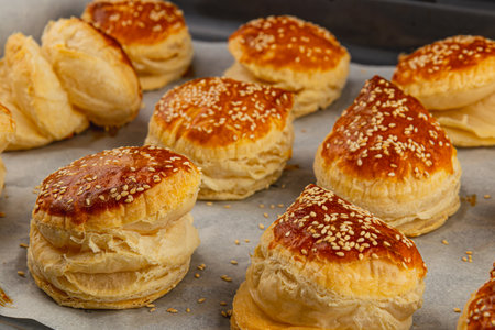 Freshly baked pastries lay on parchment paper, showcasing their flaky texture and golden brown tops. Each one is generously sprinkled with sesame seeds, inviting a tasty treat.の写真素材