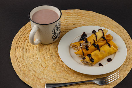 Delicious crepes filled with sweet ingredients are elegantly plated beside a cozy cup of warm chocolate drink. The setting exudes comfort and indulgence, perfect for a relaxing moment.の写真素材