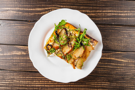 A delightful slice of homemade pizza showcases a unique combination of sweet pear and fresh arugula. Perfect for a flavorful snack. Enjoyed in a cozy kitchen setting.の写真素材