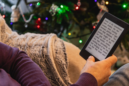 A person relaxes on a comfy couch, engrossed in an e book. Colorful lights twinkle in the...