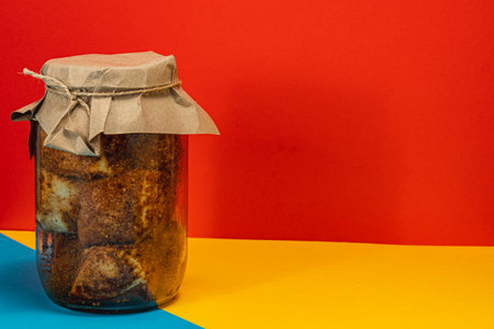 A jar filled with homemade lard and pickled beans sits against a vibrant red and yellow backdrop. The lid is covered with paper, indicating preservation methods.の写真素材