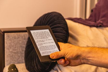 A person holds an e reader, engrossed in a digital story. The soft light creates a relaxed...