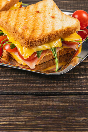 Savor a comforting grilled sandwich featuring melted cheese, succulent ham, and fresh spinach, arugula, and tomatoes, all nestled between golden toasted bread, perfect for any meal.の写真素材