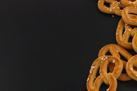 Crunchy pretzels topped with sesame seeds are arranged on a dark surface. Their golden color and unique texture create an appetizing display perfect for snacking.の写真素材