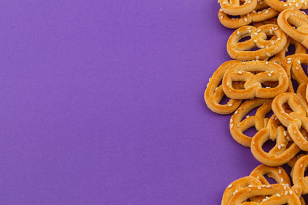Crunchy pretzels are scattered on a bright purple surface, highlighting their golden color and sesame seed topping. Perfect for snacking at any time of the day or for gatherings.の写真素材