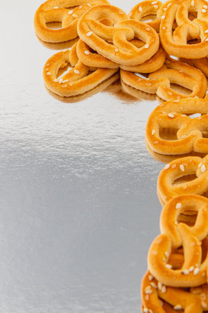 Freshly baked pretzels are neatly arranged in a delightful pattern on a shiny surface. The golden-brown treats are sprinkled with sesame seeds, creating an inviting display.の写真素材