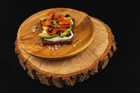 A colorful open-faced sandwich is topped with sliced tomatoes and avocado, served on a rustic wooden board. This vibrant dish showcases a healthy option perfect for lunch or a snack.の写真素材