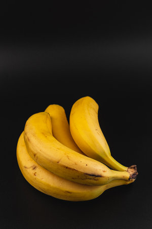 A bunch of ripe yellow bananas rests together on a contrasting dark surface, showcasing their vibrant color and smooth texture, perfect for healthy snacking or baking.の写真素材