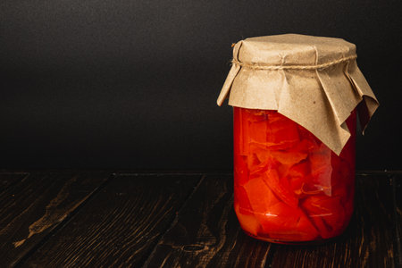 Bright red pickled tomatoes are stored in a glass jar, sealed with a paper cover. This homemade preservation reflects a local tradition of using lard and salt for flavor.の写真素材