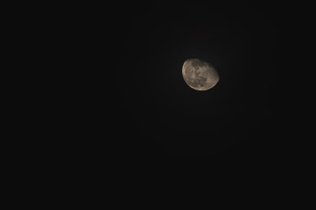 Under a dark sky, the incomplete moon glows softly as it hovers among wispy clouds, creating a...