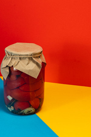 A glass jar filled with homemade pickled vegetables sits on a colorful surface. The jar is covered with brown paper, showcasing a traditional preservation method.の写真素材