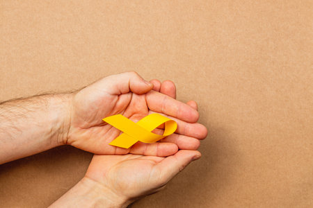 Hands gently hold a yellow awareness ribbon, symbolizing hope and support for those affected by cancer. This act represents solidarity and the fight against illness.の写真素材