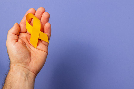 A hand holds a yellow ribbon symbolizing hope and awareness for cancer patients. This representation highlights the fight against cancer and promotes solidarity and support for those affected.の写真素材