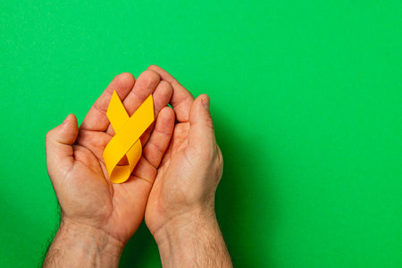 Two hands hold a bright yellow ribbon, symbolizing support and awareness for cancer, showcasing hope and solidarity against illness and the fight for life.の写真素材