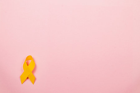 A bright yellow ribbon on a soft pink background represents hope and solidarity in the fight against cancer, encouraging awareness and prevention efforts.の写真素材