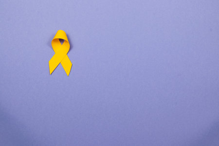 A yellow ribbon is displayed against a pastel background, representing hope and solidarity in the fight against cancer. This ribbon serves as a powerful symbol of awareness and support.の写真素材
