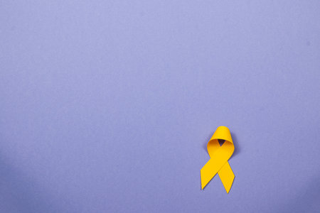 A yellow ribbon rests against a pastel background, symbolizing support for those affected by cancer....