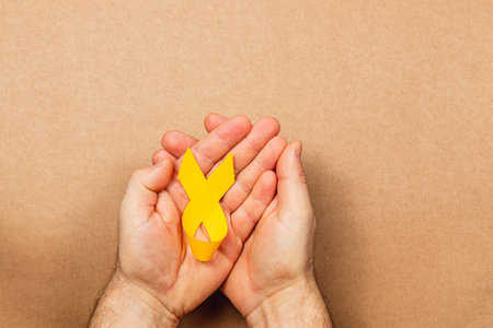 Two hands cradle a yellow ribbon, representing cancer awareness and support. This gesture embodies solidarity in the fight against illness and highlights the importance of early detection and care.の写真素材