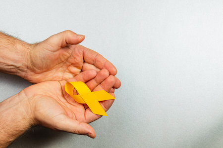 Two hands gently hold a yellow ribbon, representing solidarity in the fight against cancer. This powerful symbol embodies hope, support, and awareness in the ongoing battle against illness.の写真素材