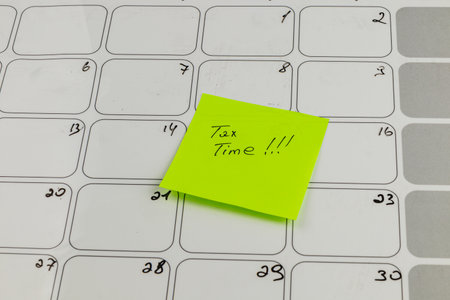 A bright yellow sticky note marked with tax time stands out on a blank calendar, highlighting the...