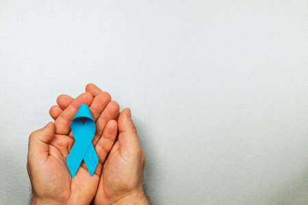 A patient holds a blue ribbon in both hands against a grey background, representing awareness and support for prostate cancer detection and prevention efforts in a healthcare setting.の写真素材