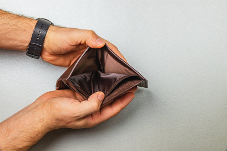 A person holds an empty wallet with both hands, revealing signs of financial distress. This visual reflects the struggles of managing expenses during difficult economic times.の写真素材