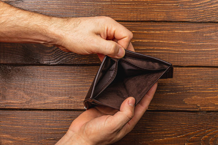 A male businessman looks worried as he inspects his empty wallet. This moment highlights feelings of despair and loss in the face of financial instability and economic hardship.の写真素材