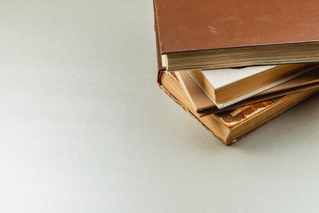 A collection of vintage books with brown and cream covers sits stacked on a light gray surface, creating a cozy reading atmosphere ideal for book lovers and collectors.の写真素材