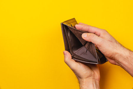 A male's hands gripping an empty leather wallet illustrate the struggle of financial crisis and...