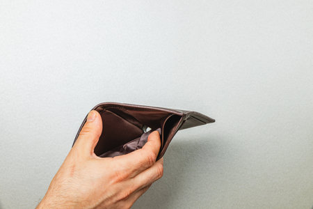 A male businessman holds an empty leather wallet, illustrating feelings of poverty and despair...