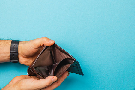 A male businessman holds an empty wallet, expressing despair over his financial situation. The stark contrast illustrates the deep impact of recession and loss on personal finances.の写真素材