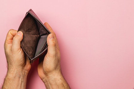 A businessman examines his empty wallet with a look of despair and disbelief, symbolizing the...