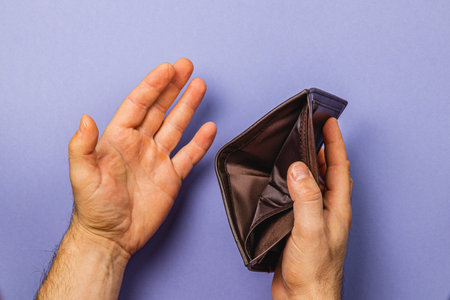 Hands grasp an empty wallet, revealing its interior against a vibrant purple background. This gesture symbolizes financial emptiness and the challenges of budget management.の写真素材