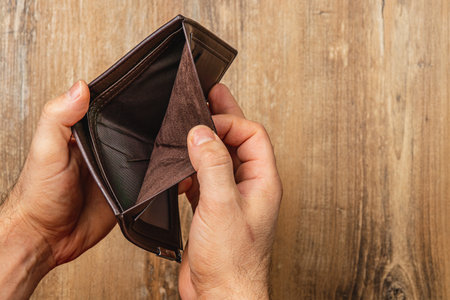 A businessman examines his empty wallet, reflecting on financial challenges.の写真素材