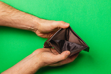 A male businessman holds an empty leather wallet with a look of worry on his face, reflecting the struggle with poverty, job loss, and budgeting in a troubled economy.の写真素材