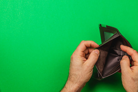 A male businessperson looks into an empty wallet, highlighting feelings of despair due to financial...