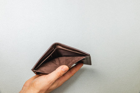 A male businessman holds an empty wallet, symbolizing financial strain and loss. The setting reflects a pressing economic downturn, highlighting themes of budgeting and job insecurity.の写真素材
