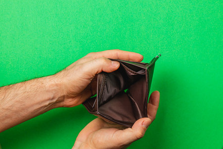 Two hands grasp a closed, empty wallet, symbolizing financial hardship. The bright green background accentuates feelings of scarcity during challenging economic times.の写真素材