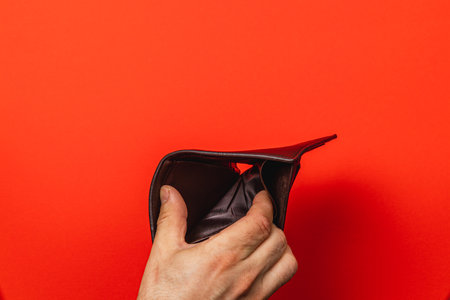 A man holds his empty leather wallet against a vibrant red background, reflecting feelings of poverty and despair amid a financial crisis. Searching for solutions, he faces a challenging future.の写真素材