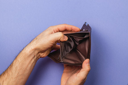 A male business professional examines his empty wallet, reflecting feelings of despair and loss. This moment illustrates the harsh reality of economic struggles and financial burdens.の写真素材