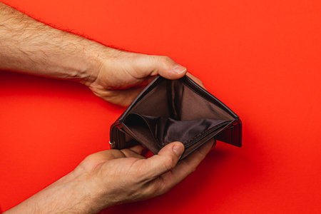 A man holds an empty wallet, symbolizing the challenges of financial management during times of recession. The stark red background highlights feelings of despair and loss.の写真素材
