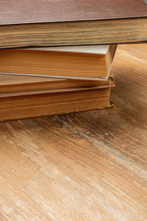 Close-up of a stack of vintage books on a rustic wooden table, showcasing their texture and color. Soft natural light enhances the warm tones of the books and wood.の写真素材