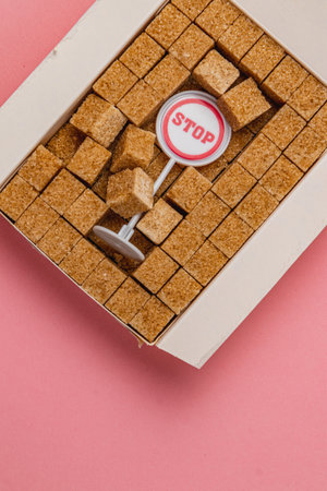 A pile of brown sugar cubes neatly arranged in a box on a soft pink surface. A small stop sign sits prominently among the cubes, adding a playful element to the composition.の写真素材