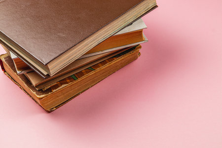 A collection of books in different colors and sizes is stacked on a pink surface. The arrangement showcases the textures and spines of the books, creating an appealing visual.の写真素材