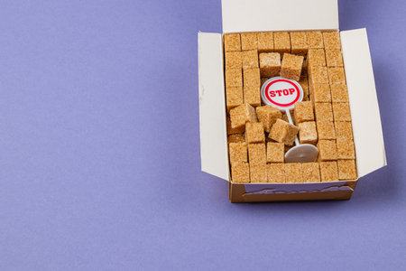 A unique arrangement of brown sugar cubes is presented in a small box. A bright red stop sign sits among the cubes, creating a playful yet striking visual against a purple background.の写真素材