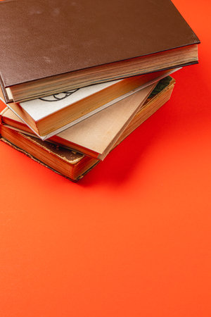 A collection of various books is stacked neatly on a bright orange surface, creating a warm and inviting atmosphere perfect for reading or studying.の写真素材