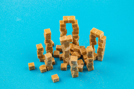 Various structures created with brown sugar cubes on a bright blue surface. Some cubes remain stacked while others lie scattered, showing texture and color contrast.の写真素材