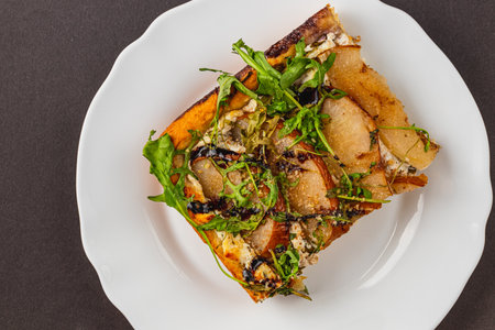 A delicious flatbread topped with slices of pear, arugula, and flavorful ingredients rests on a white plate. This culinary creation is perfect for a casual dining experience.の写真素材