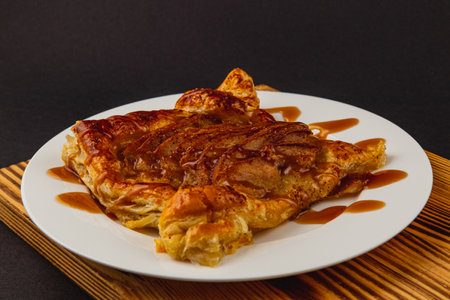 A deliciously golden pastry sits atop a wooden platter, generously drizzled with rich caramel sauce that enhances its flaky texture, inviting anyone to savor its sweetness.の写真素材