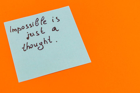 A light blue sticky note displays a message written in black ink. The vibrant orange background contrasts with the note, creating a striking visual appeal.の写真素材